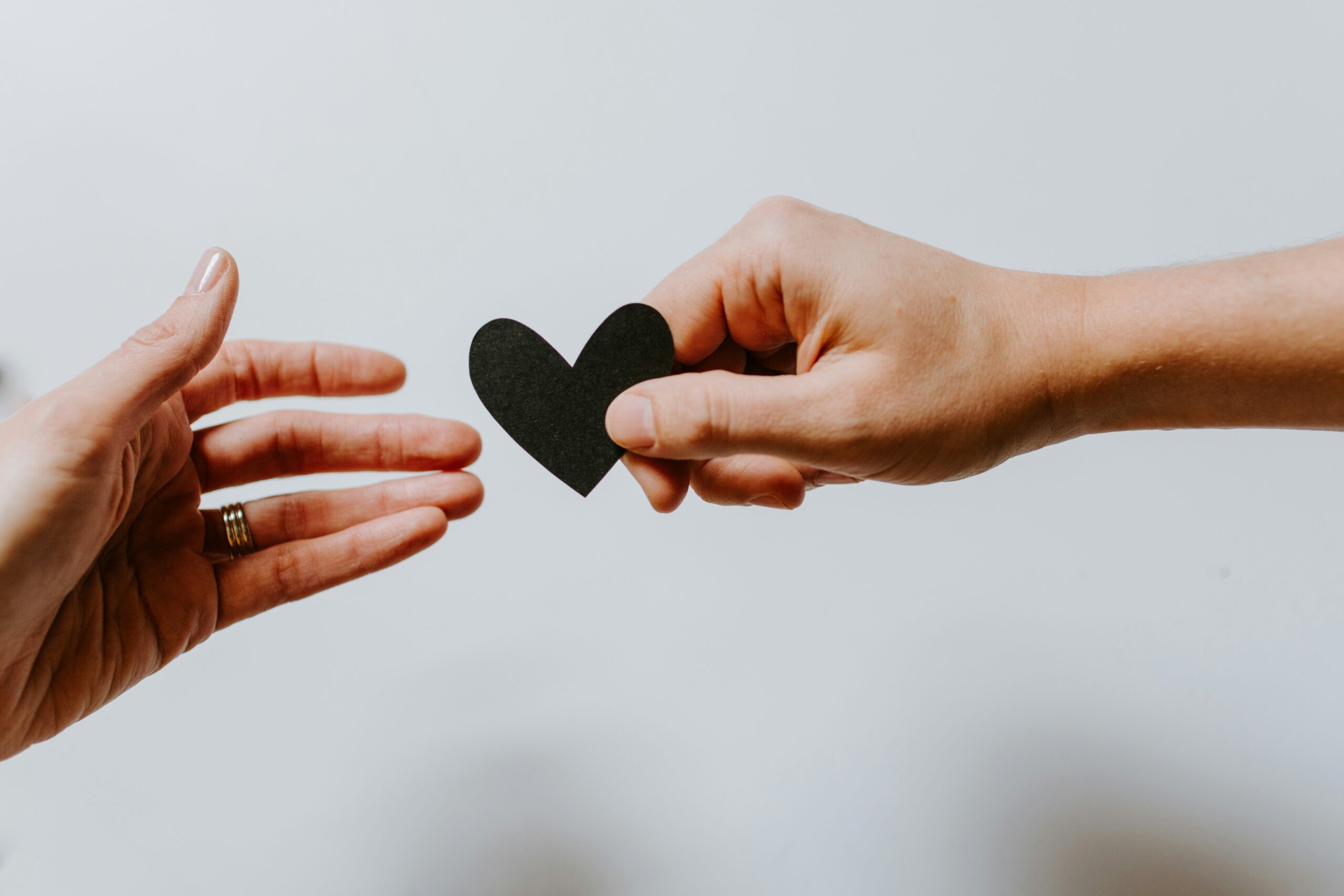 Photograph capturing two hands reaching toward each other, with one hand holding a small black paper heart.