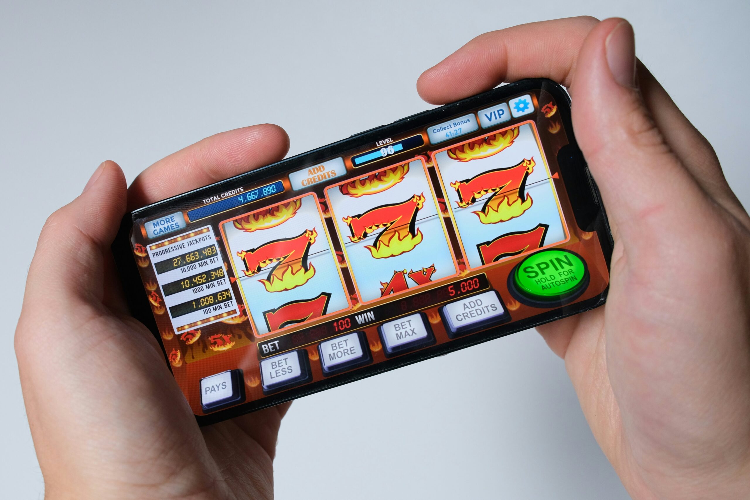 Hands holding a smartphone displaying a digital slot machine game with bull and flame symbols and a large spin button.