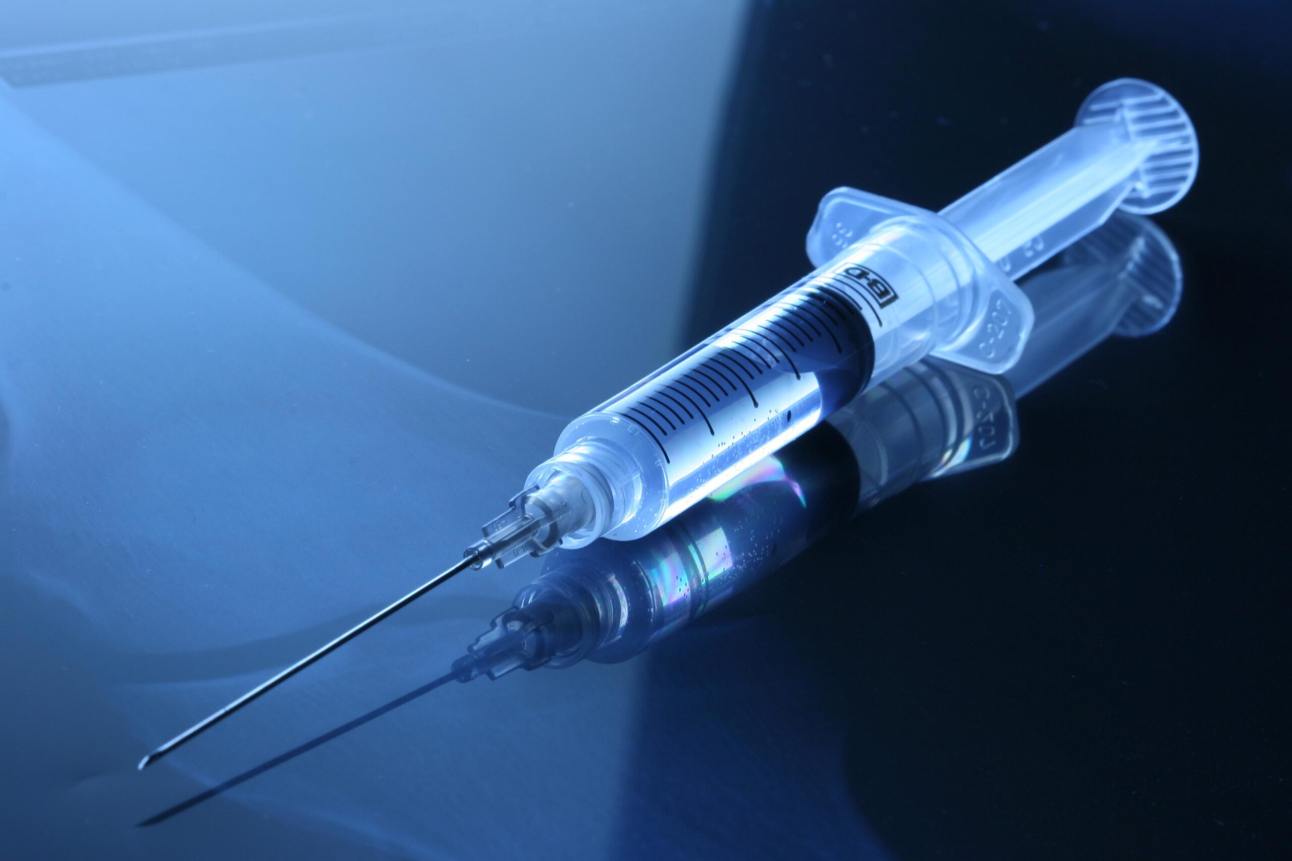 A medical syringe with a needle, positioned against a dark blue background.